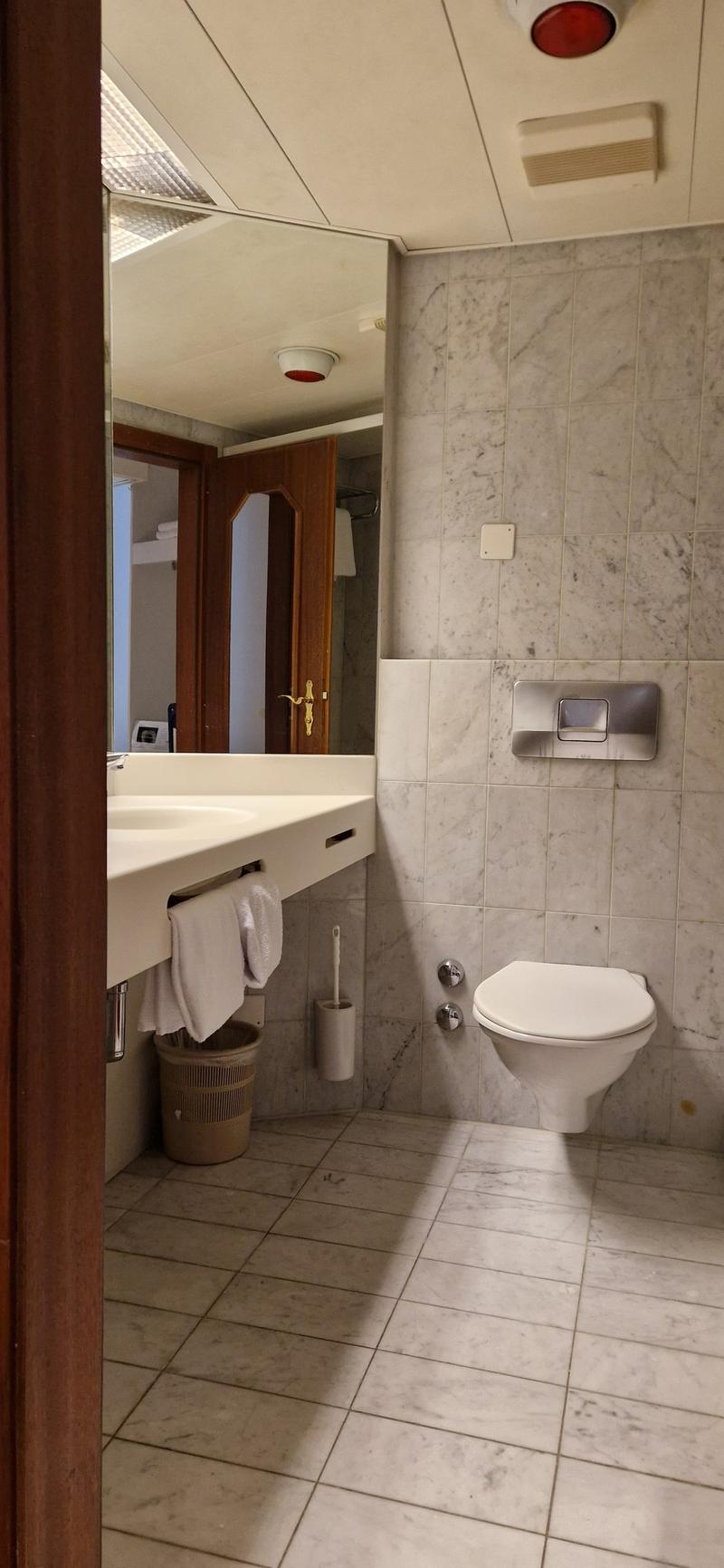 tiled floor, sink, mirror, toilet, basket, white towel, toilet brush