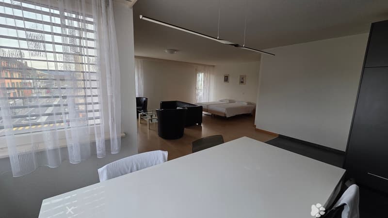 Living room with large windows, modern decor, wooden floor, two single beds, dining table and chairs, modern lamps