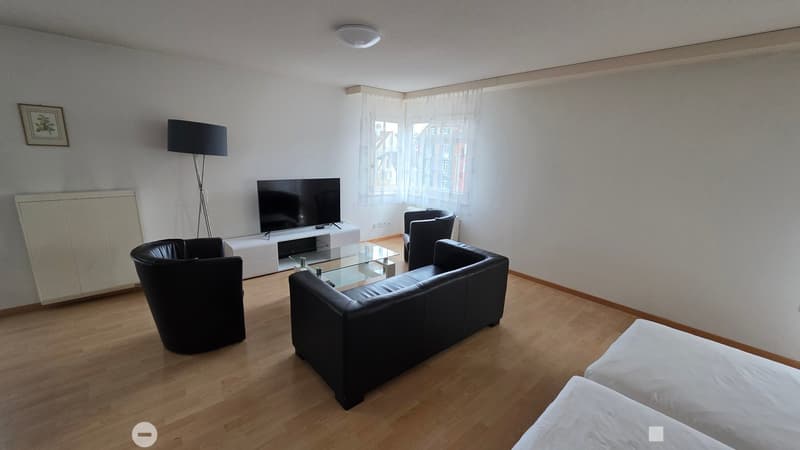 white walls, brown wood flooring, black leather couch, glass table, white tv stand, black TV, three black chairs, large window with white curtains