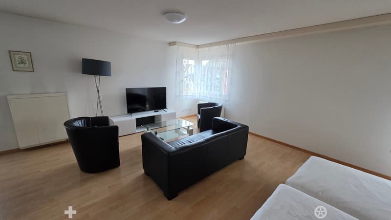 white walls, brown wood flooring, black leather couch, glass table, white tv stand, black TV, three black chairs, large window with white curtains