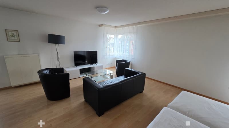 white walls, brown wood flooring, black leather couch, glass table, white tv stand, black TV, three black chairs, large window with white curtains