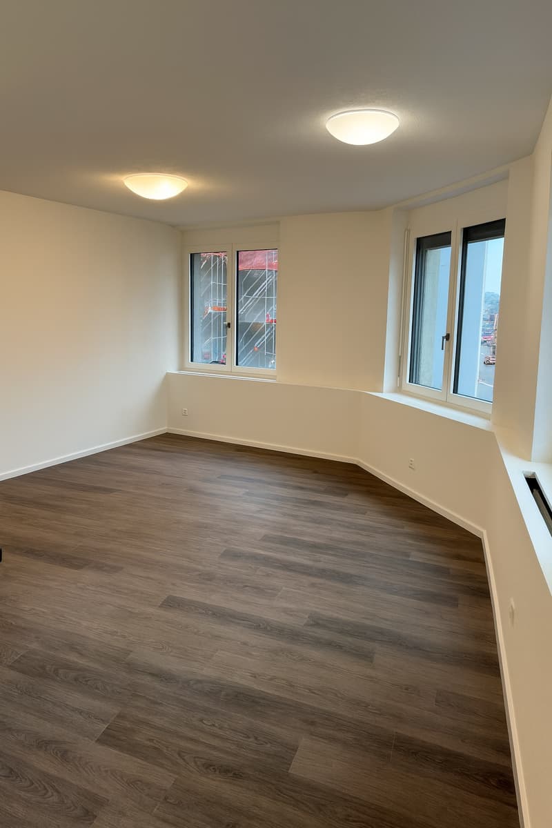 wide open room, hardwood floor, two windows, ceiling lights