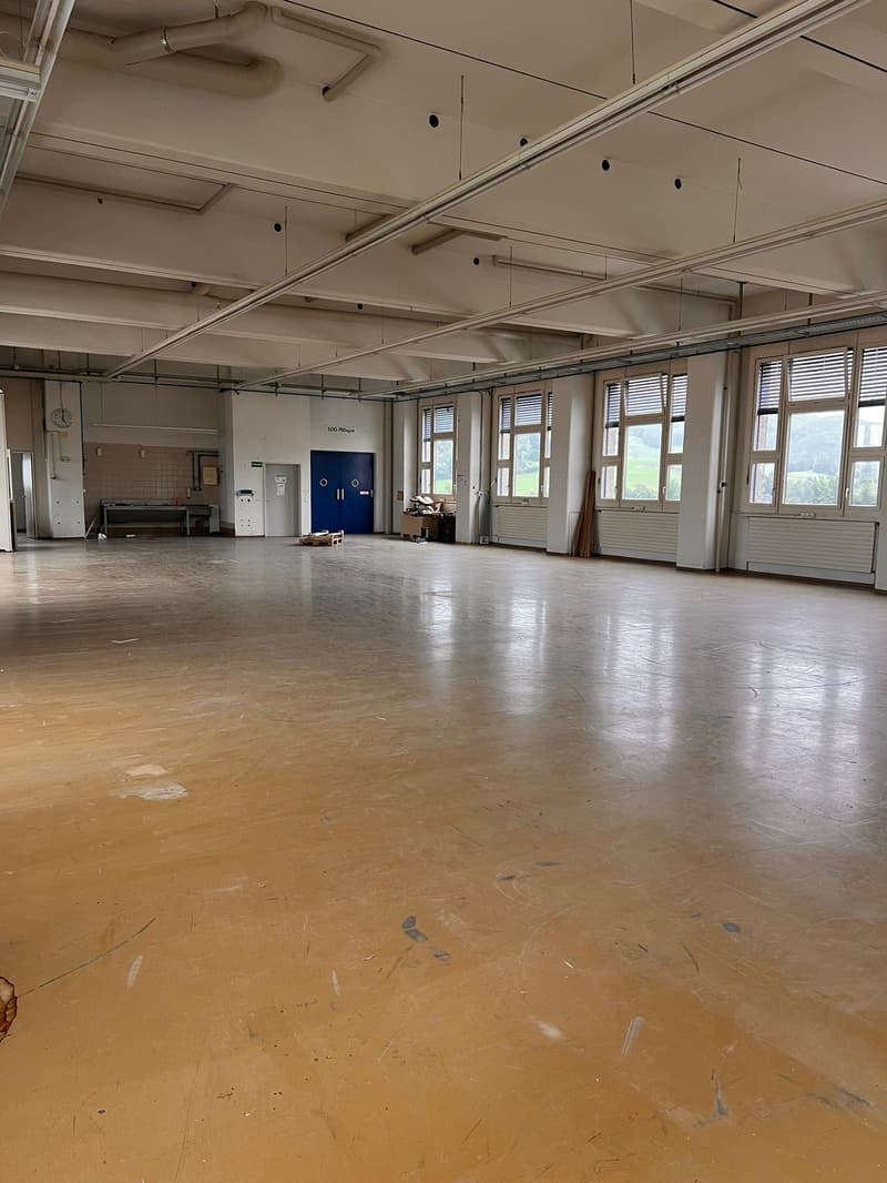 Empty room with wooden floor, white walls, blue doors, large windows with blinds, clock on the wall