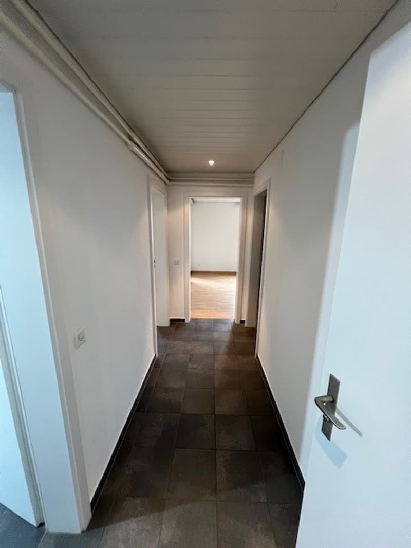 empty hallway, white walls, tiled floor, power outlet, doors leading to rooms, light on the ceiling