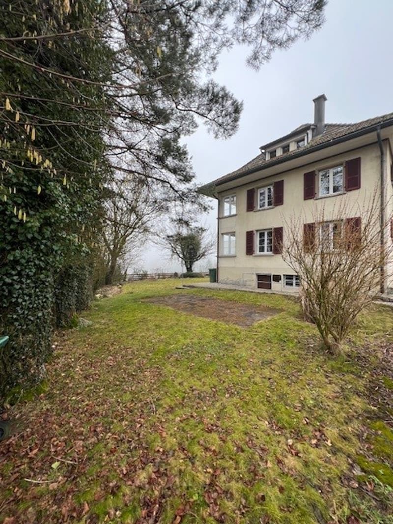 House with multiple windows, red brick, gable roof, green shrubs, large lawn