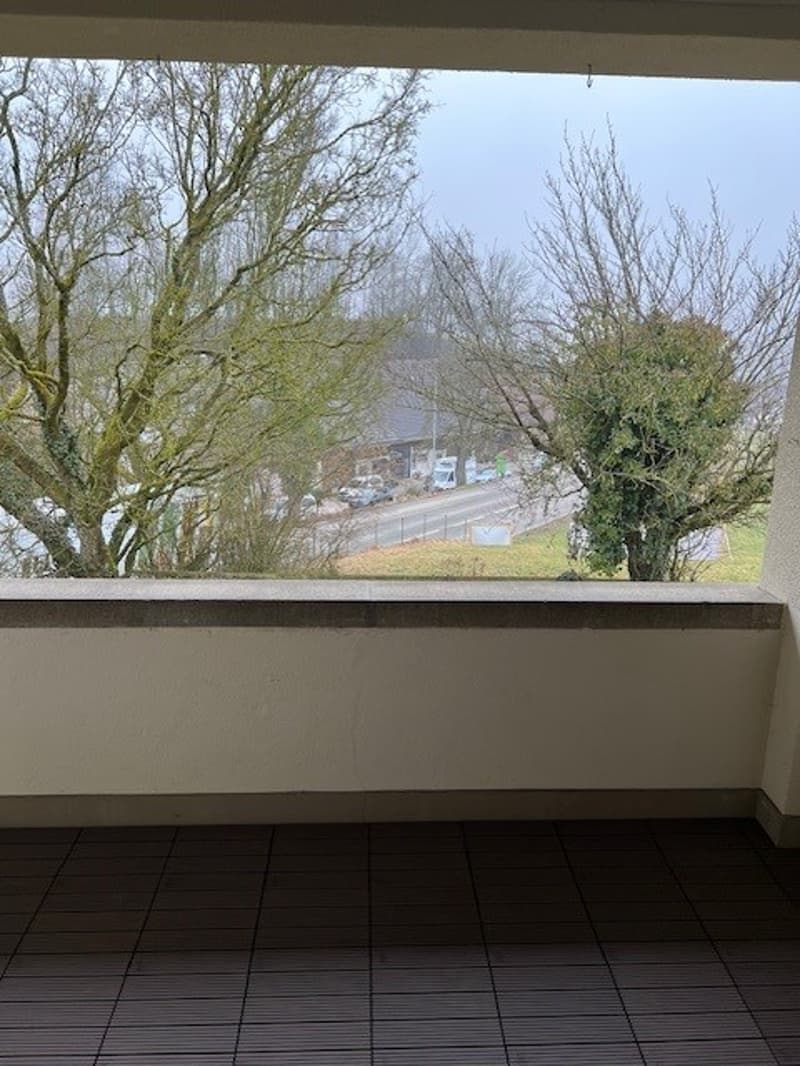 Empty balcony with a tiled floor, white wall, and a panoramic city view.