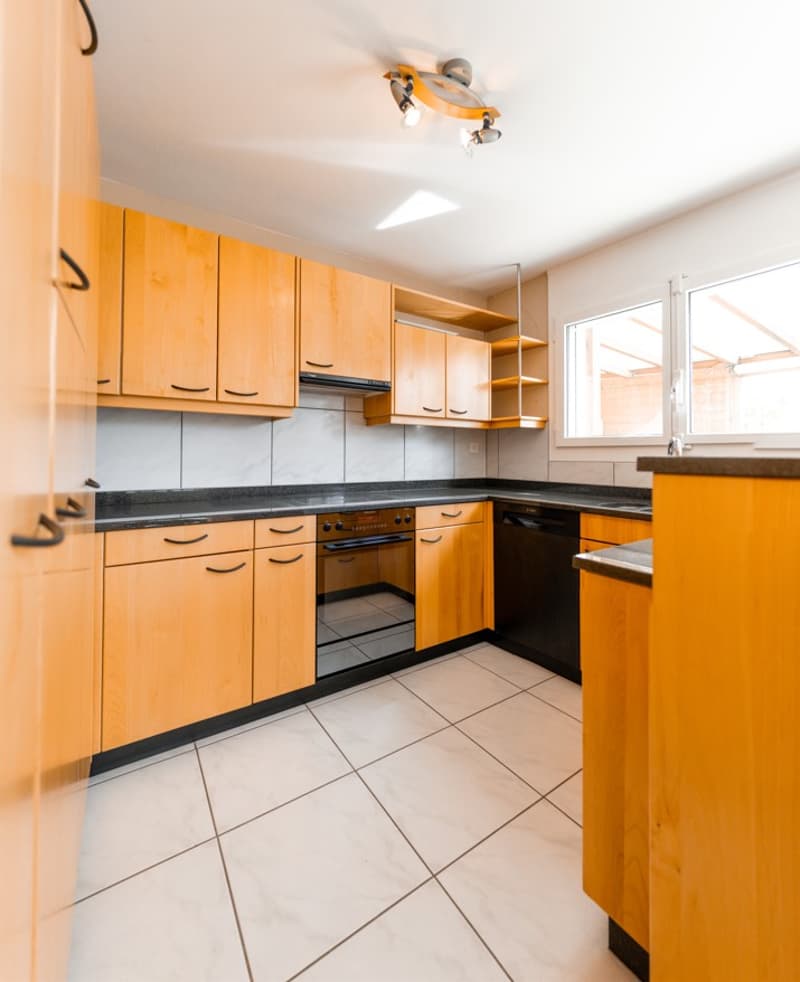 modern kitchen with wooden cabinets, black countertops, white tiles, built-in oven, dishwasher, and a window