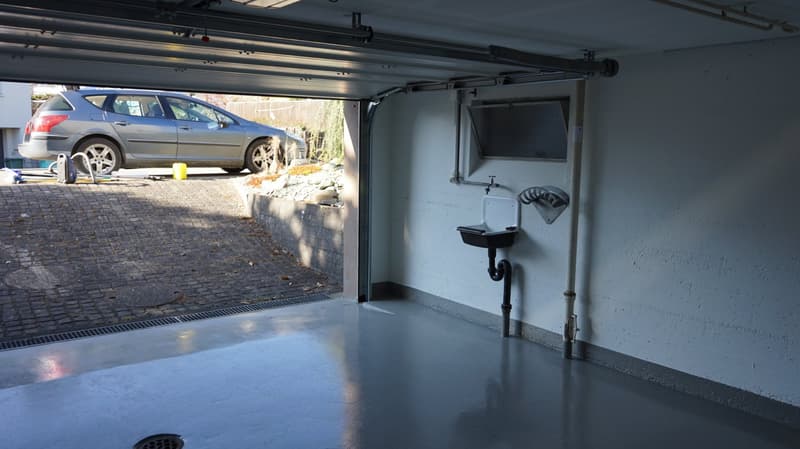 single car garage with an opening door, grey car parked, washbasin and drainpipe on wall