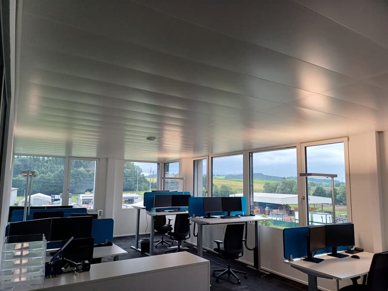 Spacious office with large windows overlooking a scenic outdoor landscape, multiple desks and computer workstations, modern and minimalist decor