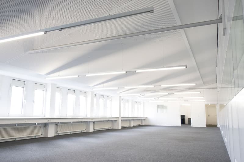 Empty room with white walls, gray floor, multiple windows, and ceiling lights