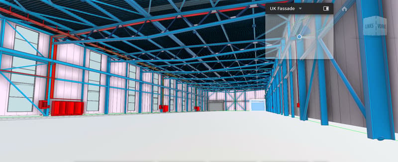 Large industrial warehouse with high ceilings, blue and red steel frame structure, multiple large windows, and a garage door visible.