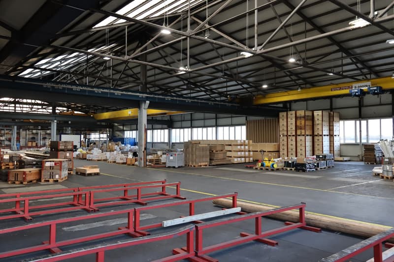 large industrial warehouse, filled with pallets and stacked boxes, high ceiling with metal frames and lighting, concrete floor, large windows
