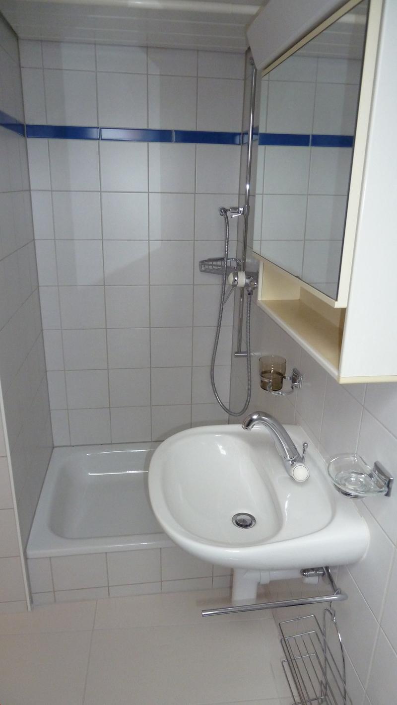 Bathroom with white tiles, bathtub, sink, mirror, and shower head.
