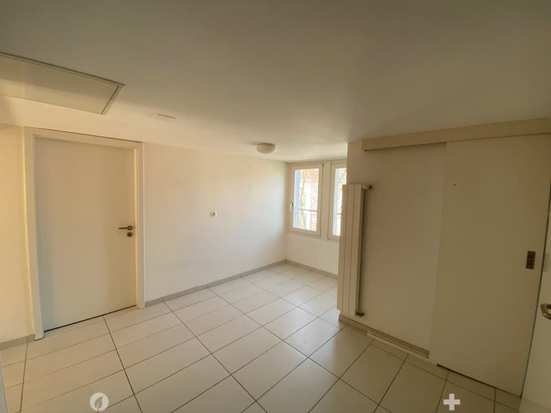 Empty room with white tiles, white walls, white doors, window with white frames, ceiling light, radiator