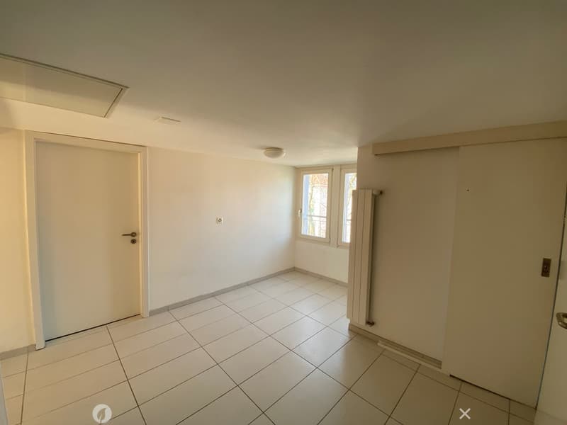 Empty room with white tiles, white walls, white doors, window with white frames, ceiling light, radiator