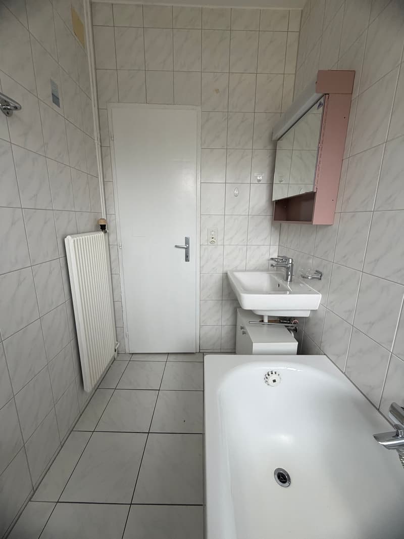 Bathroom with white tiles, white bathtub, white sink, mirror, radiator, and door