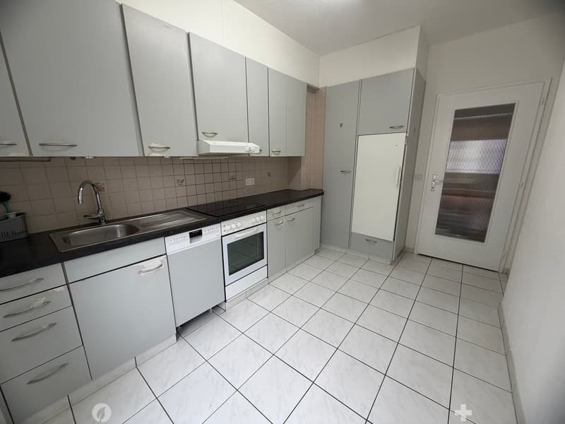 modern kitchen with white tiles, white cabinets, black countertops, stainless steel sink, dishwasher, oven, refrigerator, and a window