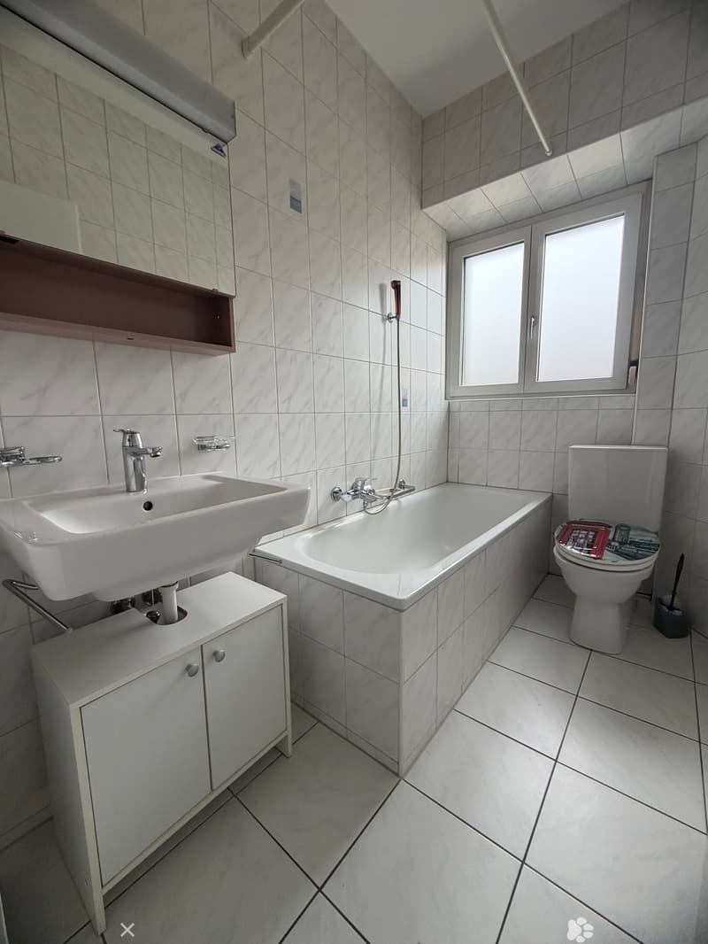 Bathroom with white tiles, bathtub, sink, toilet, and a window.