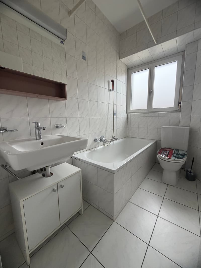 Bathroom with white tiles, bathtub, sink, toilet, and a window.