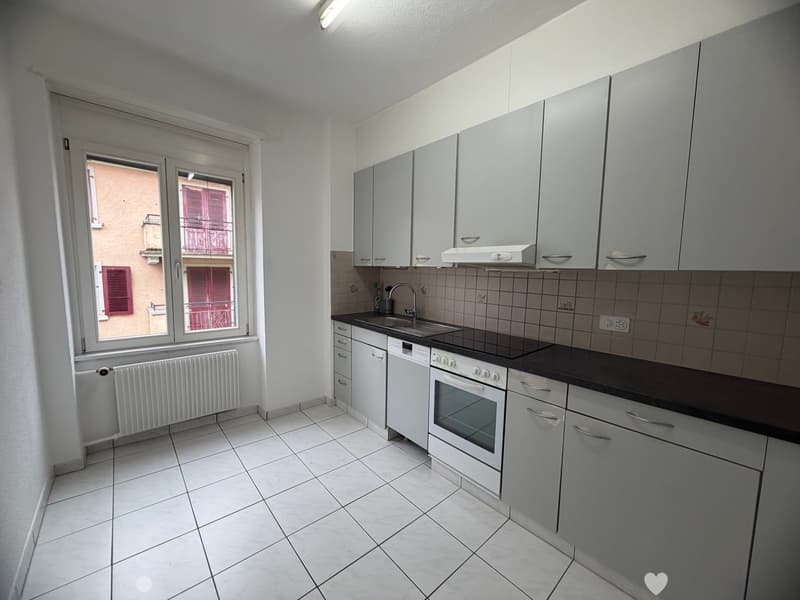 modern kitchen with white tiles, white cabinets, black countertops, white appliances, window with view to the outside