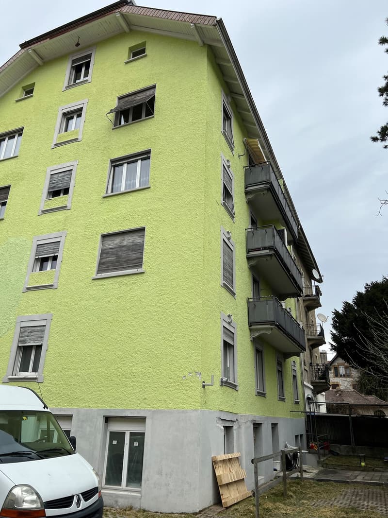 5 story building, yellow exterior, balconies, windows, white van parked in front