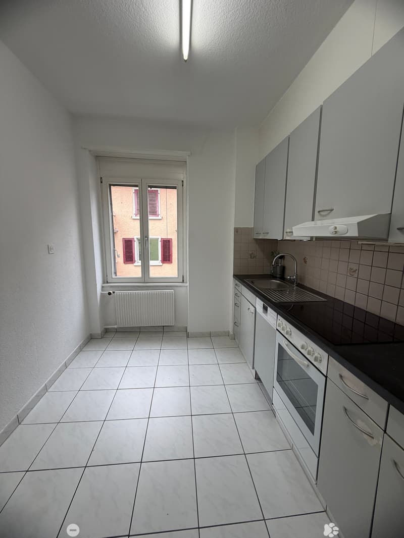 modern kitchen with white tiles, white cabinets, black countertop, white oven, sink with faucet, white washing machine