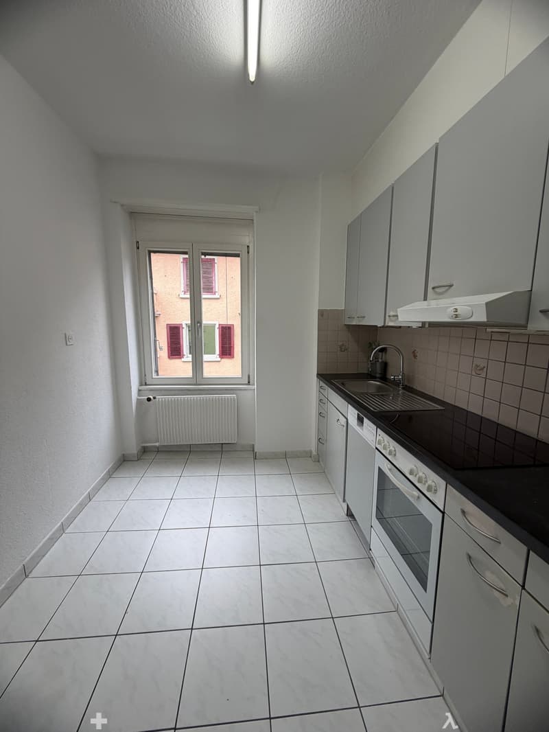 modern kitchen with white tiles, white cabinets, black countertop, white oven, sink with faucet, white washing machine