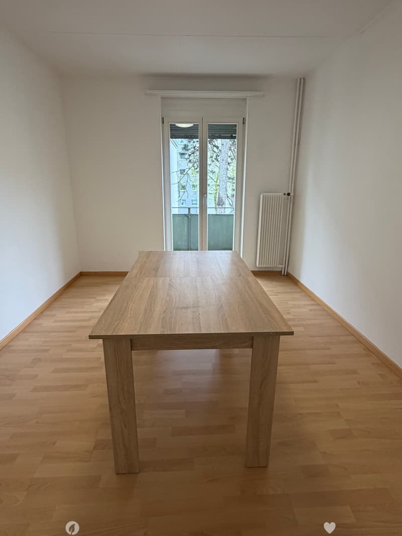 Empty room with wooden floor, large wooden table, white walls, glass door leading to a balcony