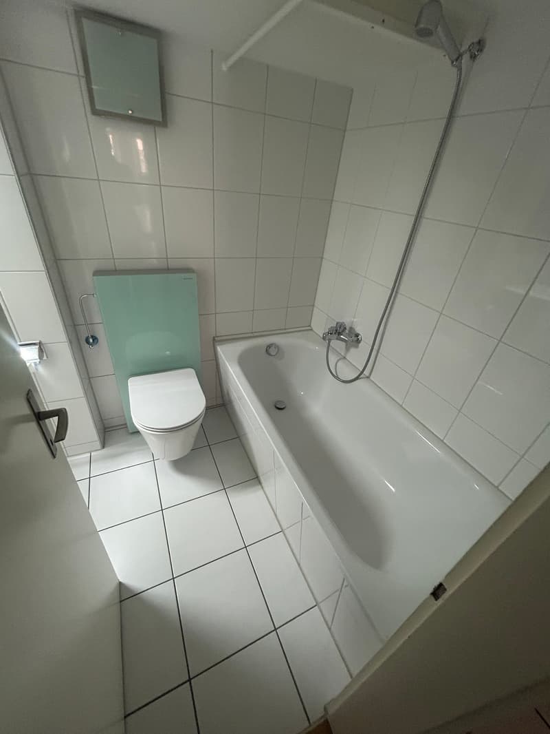 Bathroom with white tiles, white bathtub, and white toilet.