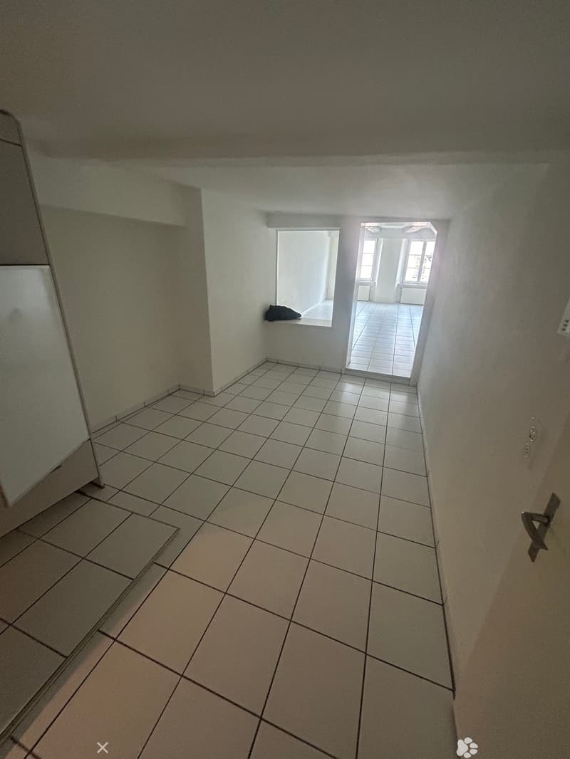an empty room with white tile flooring, a white wall, and a window with an open door