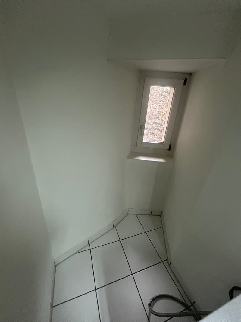 corner room with slanted ceiling, white tiled floor, small window, dark cable