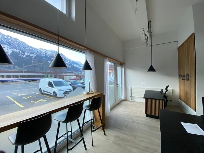 modern room with large windows, wooden floor, black chairs, desk, pendant lamps, view of mountains and parking lot
