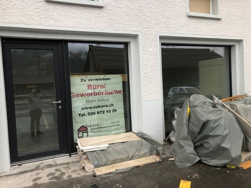 White building with glass doors, sign indicating office space for rent, construction materials outside