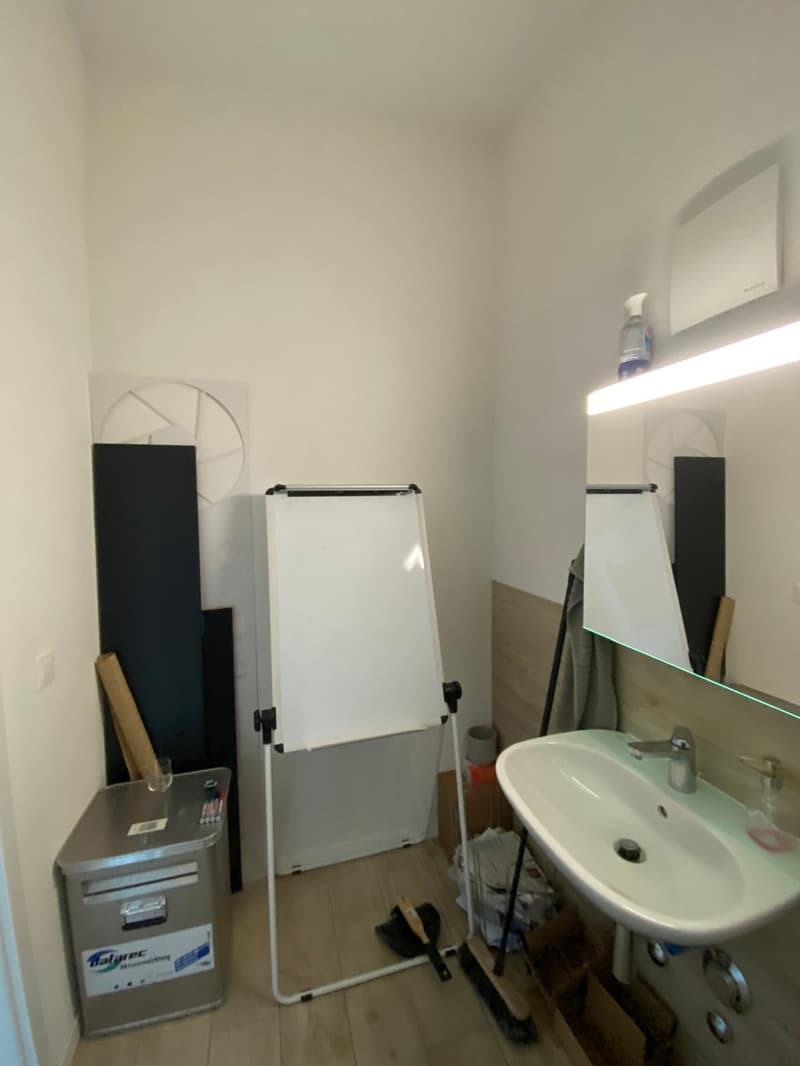 small room with sink, mirror, whiteboard, storage box, and cleaning tools