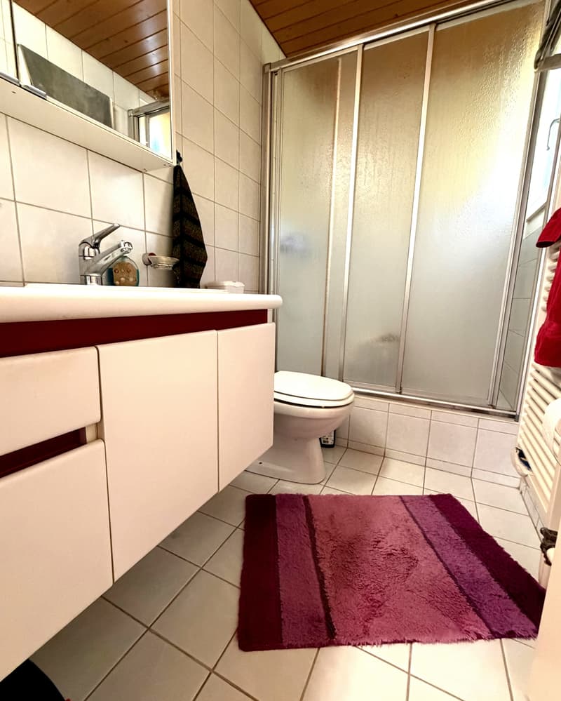 Bathroom with white tiles, white sink, white toilet, glass shower enclosure, towel rack, and a purple rug.