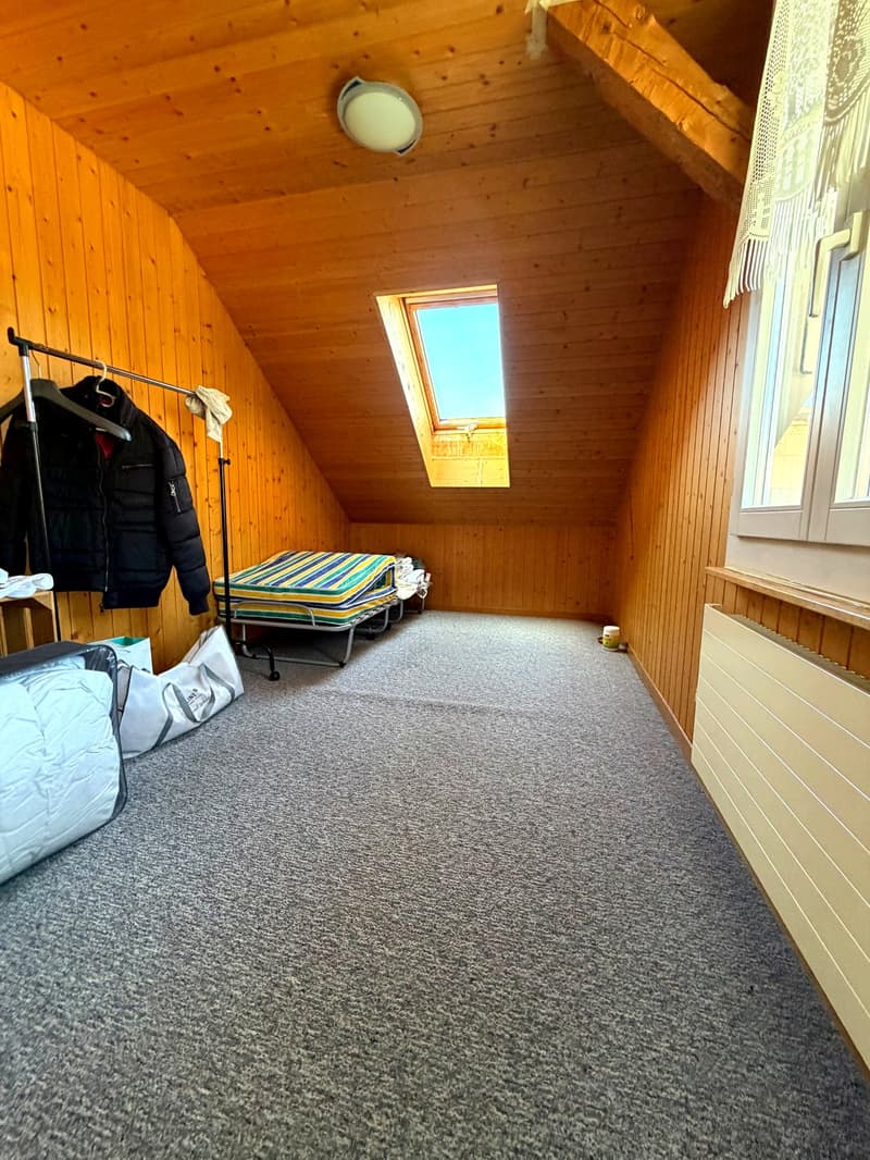 attic room with wooden walls, carpeted floor, two beds, a coat rack, a lamp, and a window