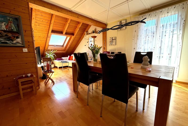 dining room with wooden floor, wooden table, black chairs, wooden stool, painting, window, flowers, couch, TV