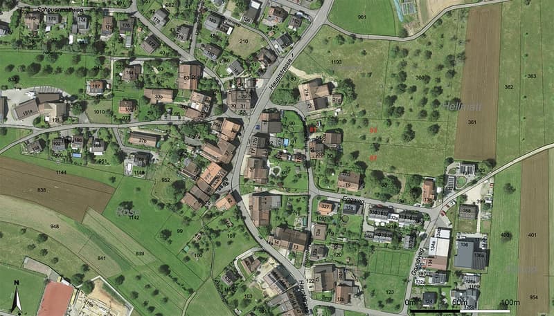 This image appears to be an aerial view or map of a residential area. It shows a town or village with various buildings, roads, and green spaces. The layout includes a mix of residential and commercial structures, as well as some open fields and wooded ar