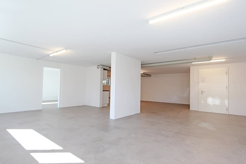Empty room with white walls and ceiling, tiled floor, recessed lighting.
