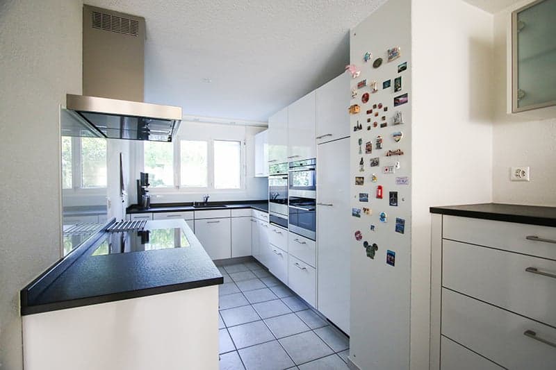 modern kitchen, white cabinets, tiled floor, stainless steel appliances, refrigerator with magnets, black countertops