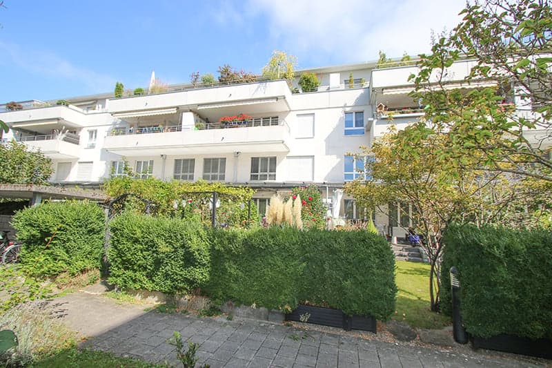 White apartment building, multiple balconies, well-maintained garden, multiple floors