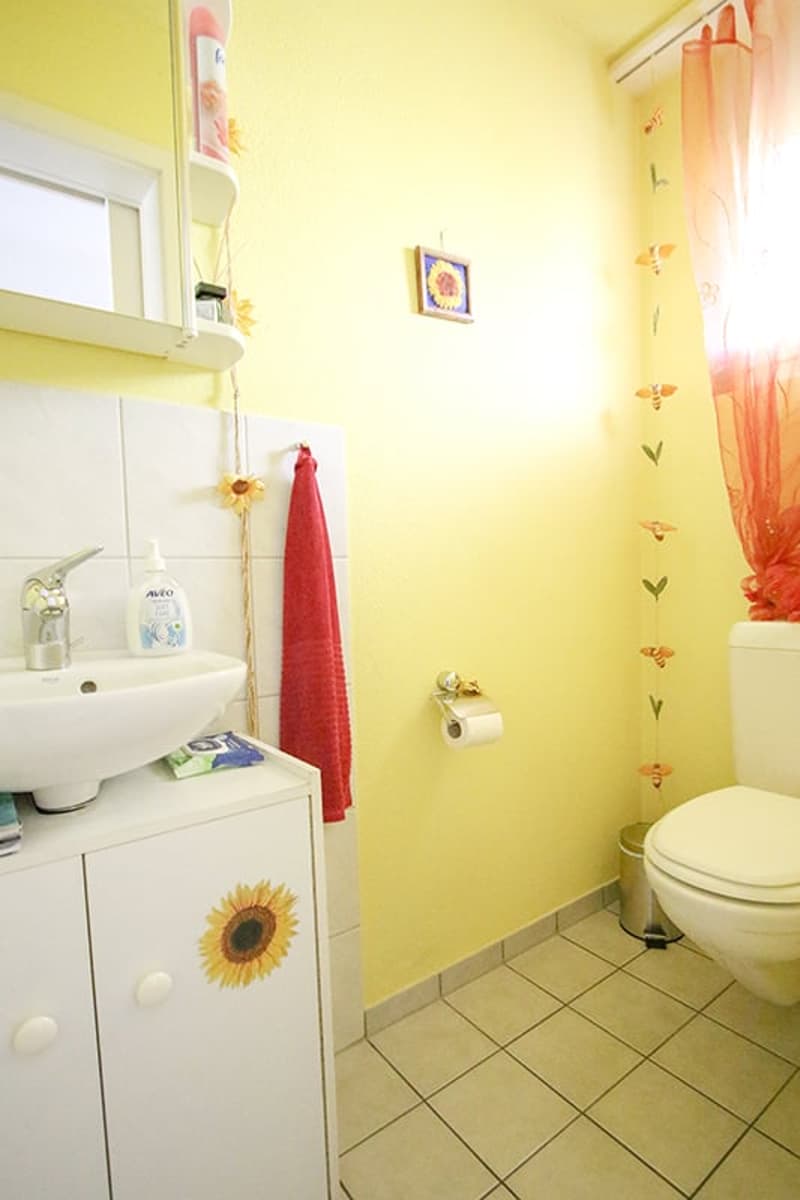 bathroom with yellow tiles, white sink, white toilet, cabinet with sunflower stickers
