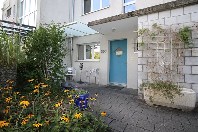 Exterior with garden area, white building, blue door, flowers, brick walls, outdoor chairs