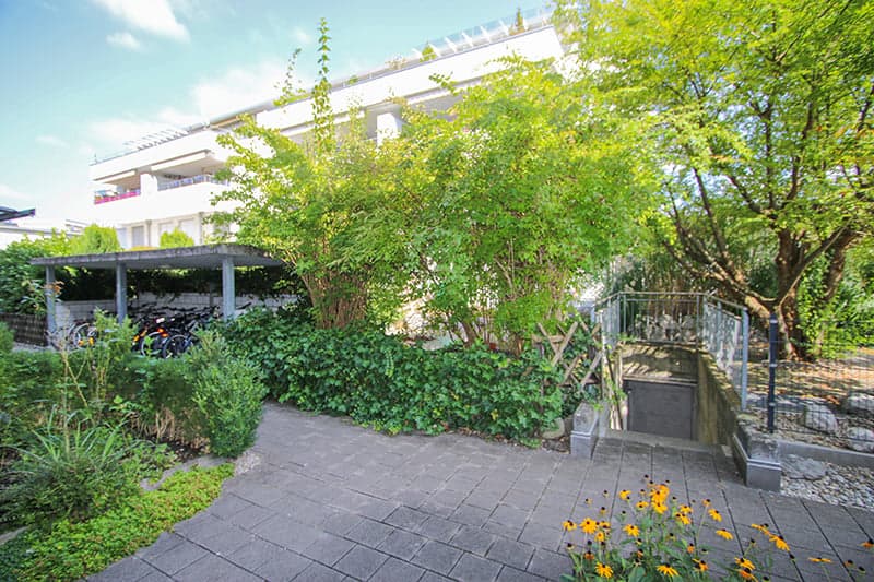 modern building, white exterior, garage entrance, plants and trees, paved pathway