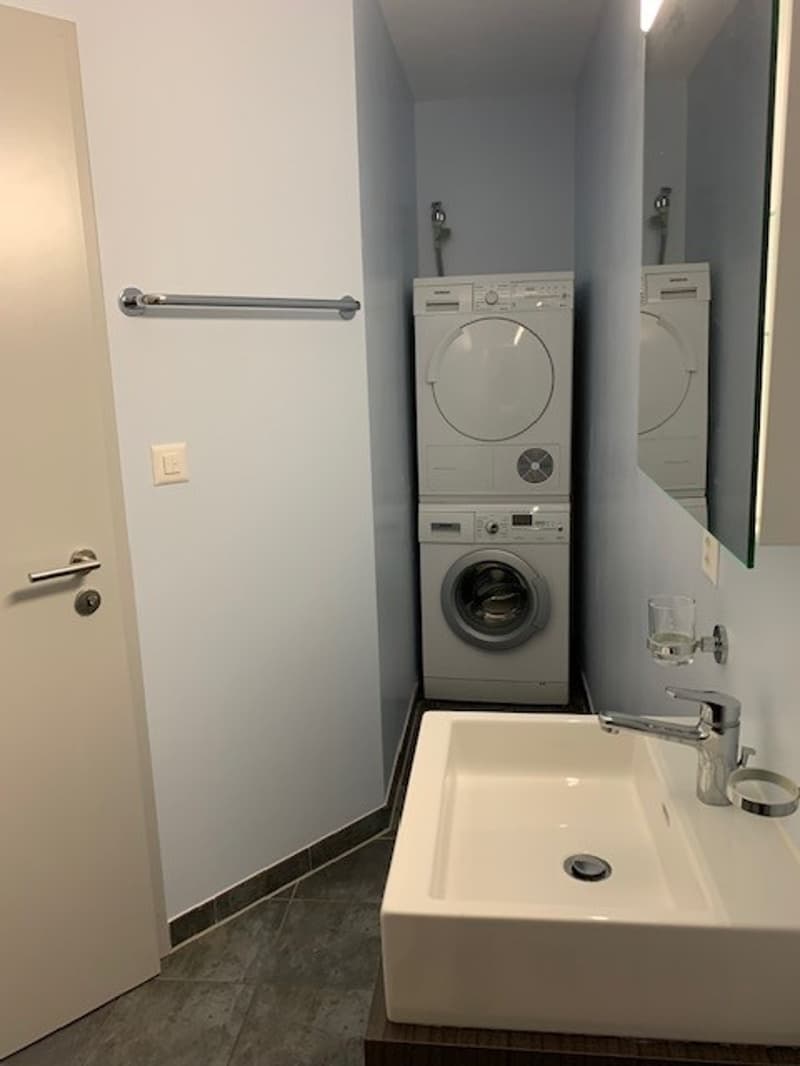 Small bathroom with a sink, mirror, and stacked washer and dryer.