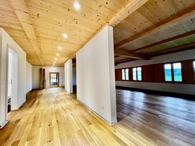 Empty room with wooden floor, white walls, wooden ceiling, windows, and doors.