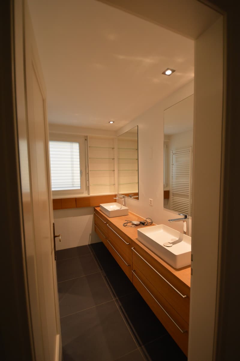 A bathroom with two vanities and mirrors, black tiles, wooden cabinets