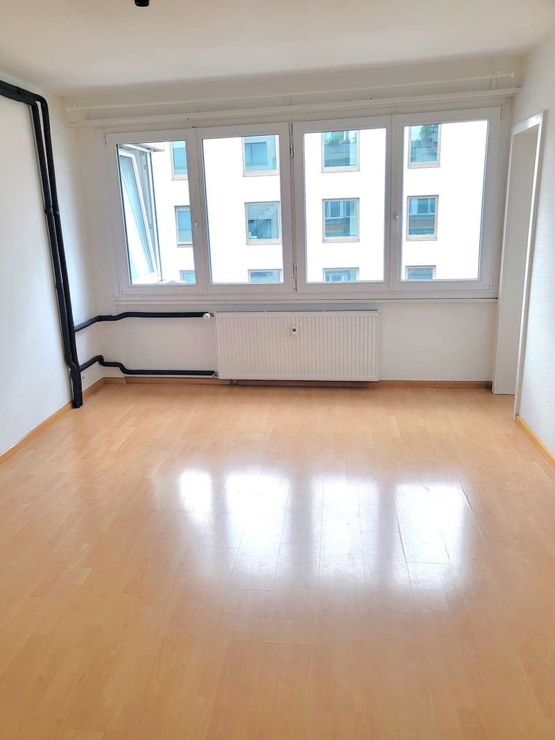 empty room with wooden floors, white walls, large windows, white radiators, pipes on the walls
