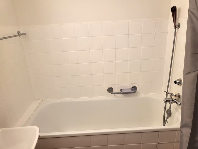 white tile walls, white tile floor, bathtub, shower head and handle, towel holder, sink