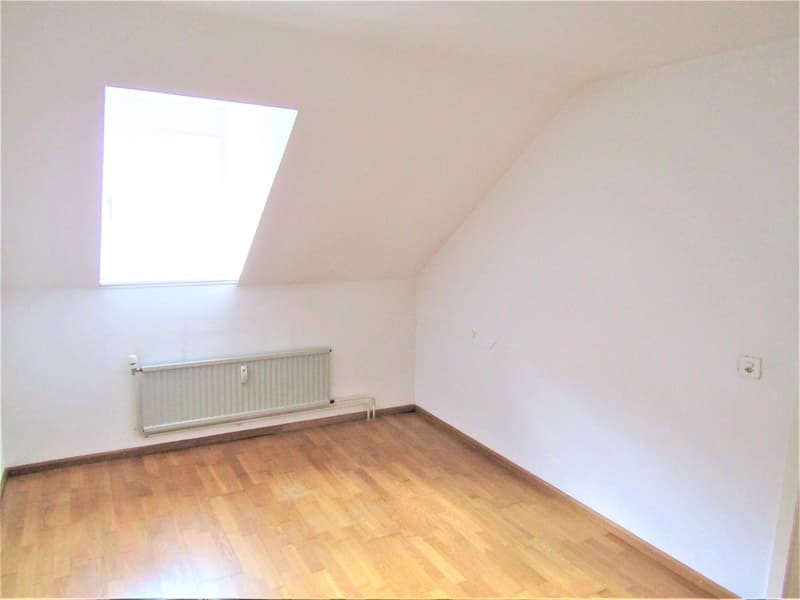 Empty room with wooden floor, white walls, a window, and a skylight window. White radiator on the wall.